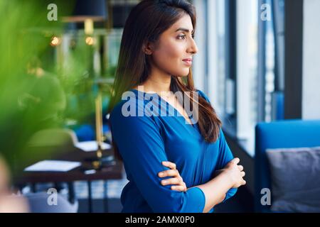 Schöne asiatische Frau, die im Büro durch Fenster schaut Stockfoto
