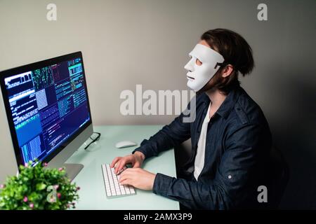 Anonymer Computerhacker in weißer Maske und Hoodie. Verdecktes dunkles Gesicht, das eine Geste zum Schweigen in der Secret Location im Underground Macht, Umgeben von Displays an Stockfoto