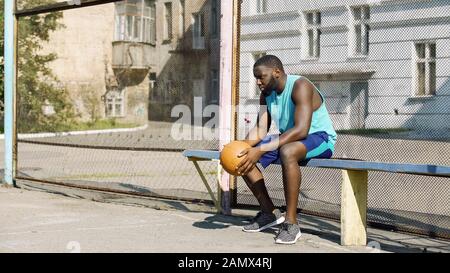 Einsame afro-amerikanische Sportlerin sitzt auf Bank und hält Ball, Depression Stockfoto
