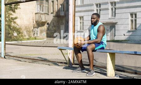 Melancholische afro-amerikanische Männer sitzen auf Bank und spielen Ball, Einsamkeit Stockfoto