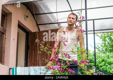 Rustikales Haus Haus Bauernhaus dacha mit jungen Mann in Europa stehend Eingang auf Klettern rosa lila Blumen Stockfoto