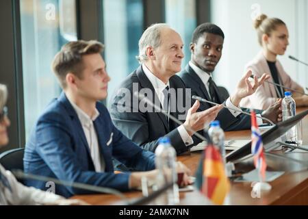 Der älteren politischen Führer in Anzug sitzen am Tisch und diskutieren einige Probleme zusammen mit seinen Kollegen an der Konferenz Stockfoto