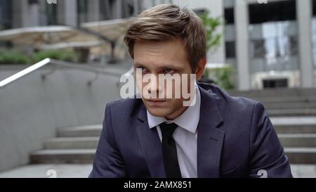 Nachdenklicher junger Mann auf dem Treppenhaus sitzend, erfolgloses Interview, Arbeitslosigkeit Stockfoto