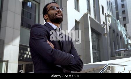 Afrikanischer Büroangestellter steht in der Nähe eines modernen Bürogebäudes und wird gefördert Stockfoto
