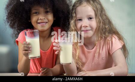 Adlige afrikanische und kaukasische Mädchen, die eine Brille Milch halten, gesunde Ernährung Stockfoto