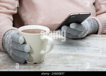 Ein Mann in warme Kleidung sitzt mit einer Tasse heißen Getränk in einem Straßencafe. Rest im Winter Sport. Eine Frau hält ein Handy in der Hand. Close-up Stockfoto