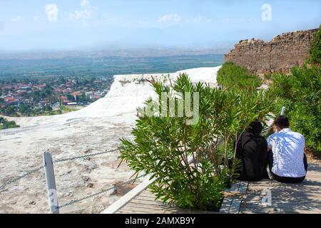Ansicht von hinten von einem Mann und einer Frau in muslimischen Kleidung, die das Sitzen auf einem hölzernen Treppe sind vor dem Hintergrund der atemberaubenden Landschaft von Pamukkale. Rest Stockfoto