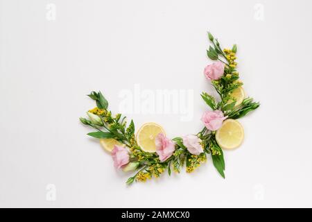 Kreative Anordnung von rosa und gelben Blumen mit Zitronen auf weißem Hintergrund mit einem Kopierraum Stockfoto