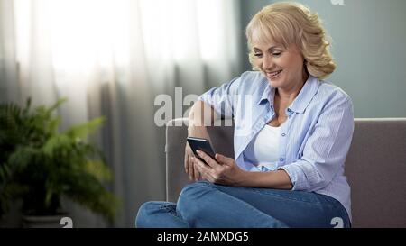 Fröhliche Frauen mittleren Alters sitzen auf der Couch und sehen lustige Fotos auf dem Telefon Stockfoto