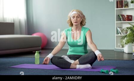 Reife Dame, die zu Hause Yoga praktiziert, Entspannungsübungen macht, Meditation Stockfoto