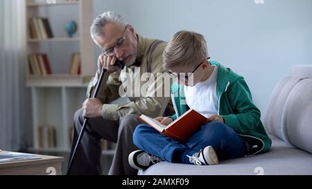 Junge in Brille Lesebuch für Großvater, alter Mann auf gemütlichem Sofa einschlafen Stockfoto