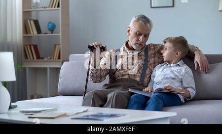 Opa beobachtet Fotoalbum mit Grandson und erinnert sich an Geschichten aus glücklicher Jugend Stockfoto