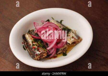 Sardinen escabeche mit frischen Kräutern mit marinierter rote Zwiebeln in weiße, ovale Platte abgedeckt Stockfoto