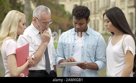 Studenten, die ihrem Lehrer eine Tablet-PC-Präsentation zeigen und über das Projekt diskutieren Stockfoto