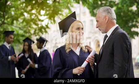 Fröhlicher blonder Diplomstudent freute sich über das Diplom mit Vater, Abschlussfeier Stockfoto