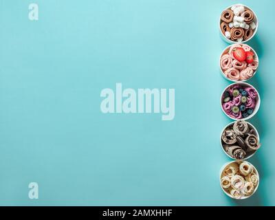 Eiscremes in Papierkonusbechern auf blauem Hintergrund. Verschiedene Eisrollen, Draufsicht oder flache Lage. Thailändisches Eiscreme mit Platz für Text oder Design Stockfoto