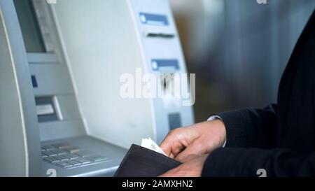 Männliche Hände legen Banknoten in die Geldbörse, nehmen Geld vom Bankkonto ab, Geldautomaten Stockfoto