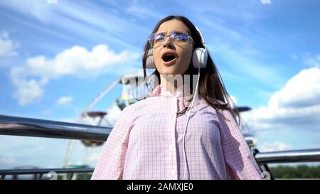 Fröhliche Brunette-Frau in Kopfhörern Musik hören und am Pier singen, Spaß Stockfoto