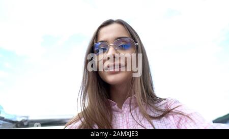 Stilvolle junge Frau in Sonnenbrille lächelt gegen Himmel und nimmt selfie, Jugend Stockfoto