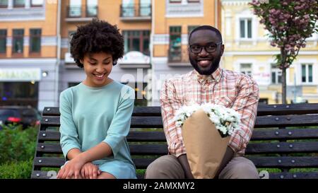 Peinlich versetzte Paare, die mit Blumen auf der Bank sitzen, erstes Datum, Zuneigung Emotionen Stockfoto