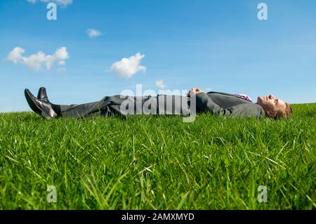 Entspannt Geschäftsmann lag auf dem Rücken auf einem sonnigen Flecken von hellem grün Gras in einem Feld mit blauem Himmel Stockfoto