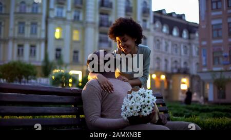 Frau umarmt Freund, mit Liebe aussehend, Blumen hält, romantisches Datum Stockfoto