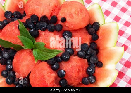 Frischer hausgemachter Wassermelon-Obstsalat mit gefrorenen Blaubeeren und Stevia-Blättern als Pfennig in einer dekorativen Rindenschale. Stockfoto