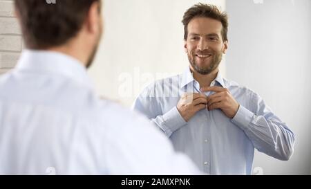 Selbstbewusster Mann knopfft sein Hemd in optimistischer Stimmung und ist bereit für die Arbeit Stockfoto