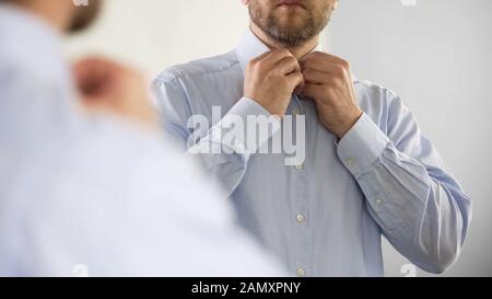 Ernster Mann knabelt sein Hemd in optimistischer Stimmung und ist bereit für die Arbeit Stockfoto
