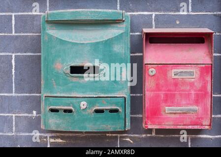 Ein grüner und ein roter alter Briefkasten an einer Ziegelwand Stockfoto