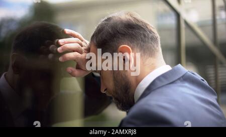 Nachdenkliche Männer lehnen sich an die Bürowand, Problem mit Arbeitsausfällen, Enttäuschung Stockfoto