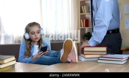 Ungehorsames Mädchen in Kopfhörern, das Musik auf dem Smartphone hört und Papa ignoriert Stockfoto