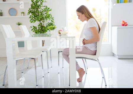 Profil Foto der hübschen Hausfrau holding Bauch leiden schreckliche Schmerzen kann nicht essen Milch frühstück Cornflakes haben magenverstimmung Sitzung Tabelle weiß Stockfoto