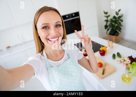 Foto der hübschen Hausfrau Wochenende Morgen kochen mit v-Werbetechnik selfies präsentieren Anhänger traditionellen Familienrezept Mahlzeit weiß Küche Stockfoto