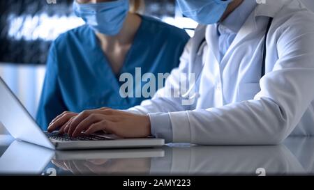 Ärzte, die Testergebnisse mit einem Laborlaptop online in medizinischen Aufzeichnungen ausfüllen Stockfoto