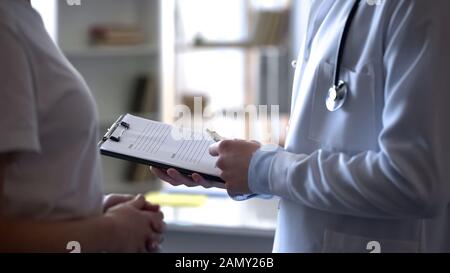 Arzt hört Beschwerden von weiblichen Patienten und schreibt sich in medizinischer Form auf Stockfoto