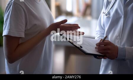 Arzt, der Patienten aufzeichnet, Beschwerden bei Kartenmädchen, die sich über gesundheitliche Probleme beschweren Stockfoto