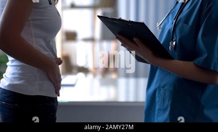 Junge Dame beklagt sich beim Schmerzarzt im Unterbauch, dem prämenstruellen Syndrom Stockfoto