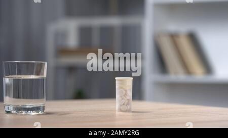 Röhrchen mit Pillen und Glas Wasser auf dem Tisch stehen, Depressionsbehandlung Stockfoto