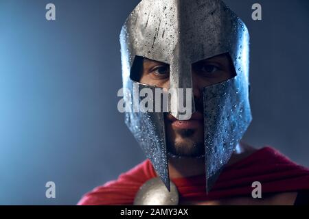 Portrait von spartanischen Krieger stehen und von der Kamera. Nahaufnahme von reifer Mann im roten Mantel und Helm mit Wassertropfen in dunklen Atmosphäre posieren. Antike Sparta, Krieger Konzept. Stockfoto