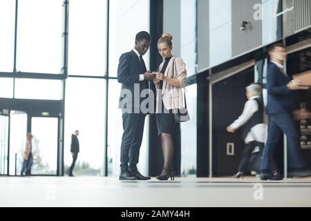 Zwei Geschäftspartner über ihre Mobiltelefone während in der Halle der Bürogebäude stehend Stockfoto