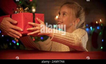 Nettes lächelndes Mädchen, das Weihnachtsgeschenk von einem Mitarbeiter des schnellen Lieferdienstes erhält Stockfoto