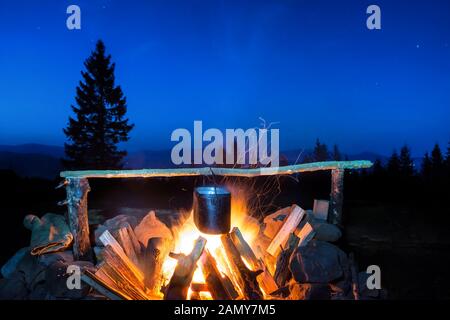 Kochen in den Topf auf dem Feuer unter blauen Nachthimmel mit vielen stars Stockfoto