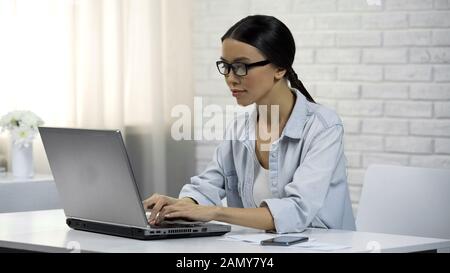 Junge asiatische Frau, die auf Laptop tippt und auf einer datingwebsite flirtige Nachricht schreibt Stockfoto