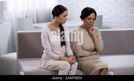 Traurige asiatische Frauen, die auf der Couch sitzen, denken über Probleme, freundschaftliche Beziehungen nach Stockfoto
