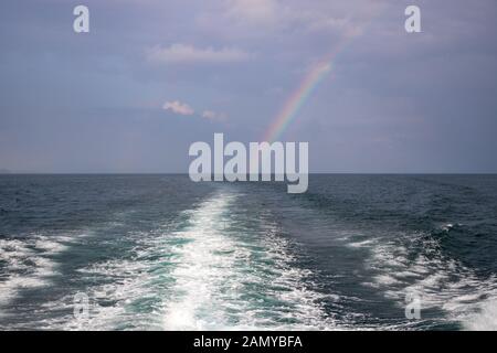 Wellen aus einem Boot segeln mit Regenbogen in der Kulisse im Andaman Meer vor der Küste von Thailand in der Stadt Krabi Stockfoto