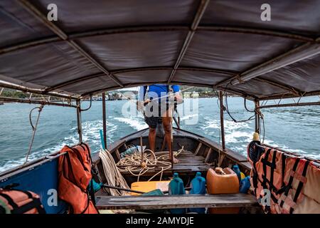 Innen in der thailändischen Longtail Boot. Blick auf leere Sitzplätze für Passagiere und Schwimmwesten. Die Sailor steuert das Boot und Segel von der Küste auf das Meer Stockfoto