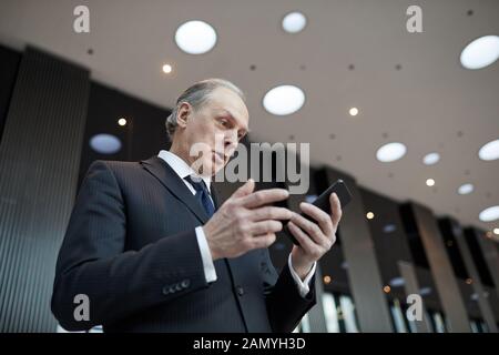 Ernst senior Geschäftsmann in Anzug mit seinem Handy, während moderne Büro stehend Stockfoto