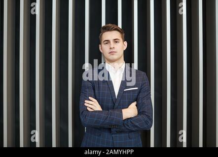 Porträt der jungen zuversichtlich Geschäftsmann im Anzug stand mit verschränkten Armen und Kamera im Freien Stockfoto