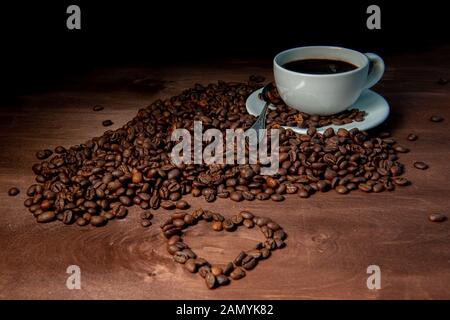 White Coffee Mug und Kaffeebohnen auf dem dunklen Hintergrund, Herzform aus Kaffeebohnen im Vordergrund - Bild Stockfoto